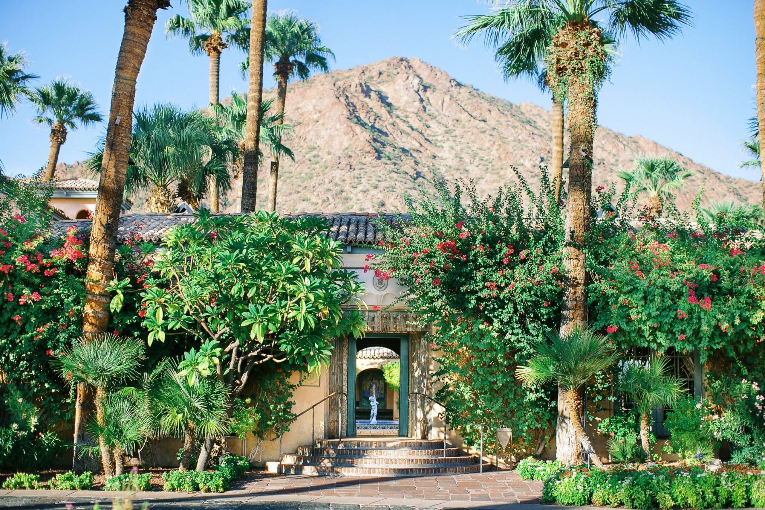 Garden entrance of the Royal Palms Resort and Spa framed by palm trees and bougainvillea, with Camelback Mountain rising behind it
