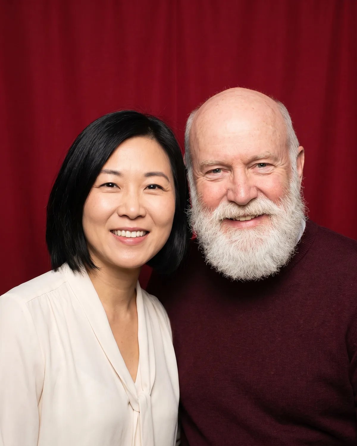 A young woman with a black bob and an older bald man with a white beard at a holiday party