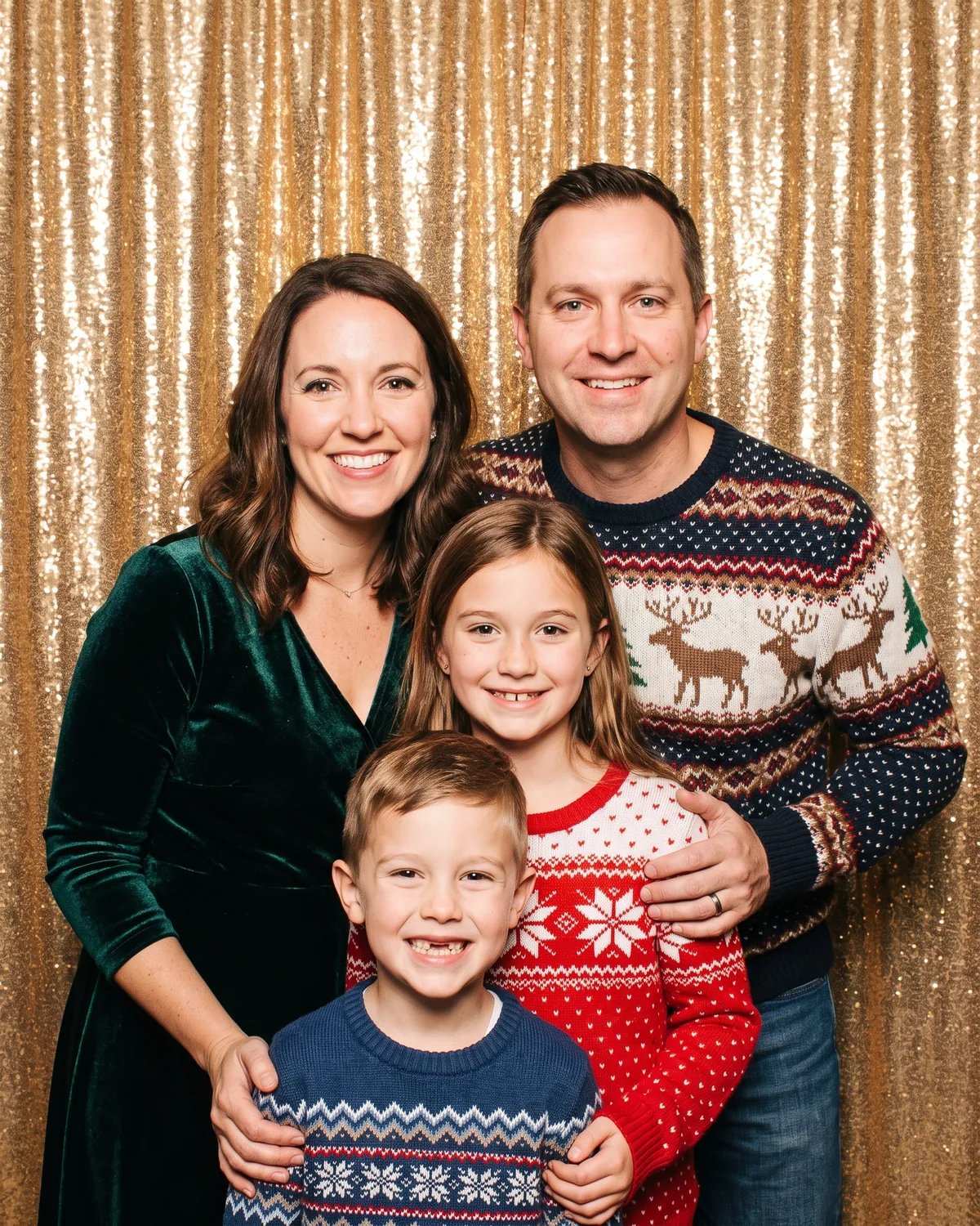 A family of four in holiday sweaters in front of a gold sequin backdrop