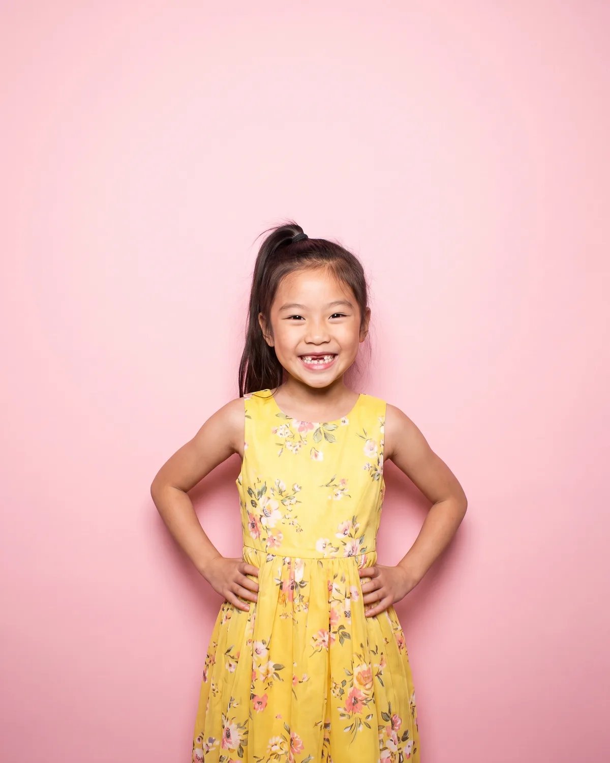 A girl at her birthday party in a yellow dress, hands on her hips