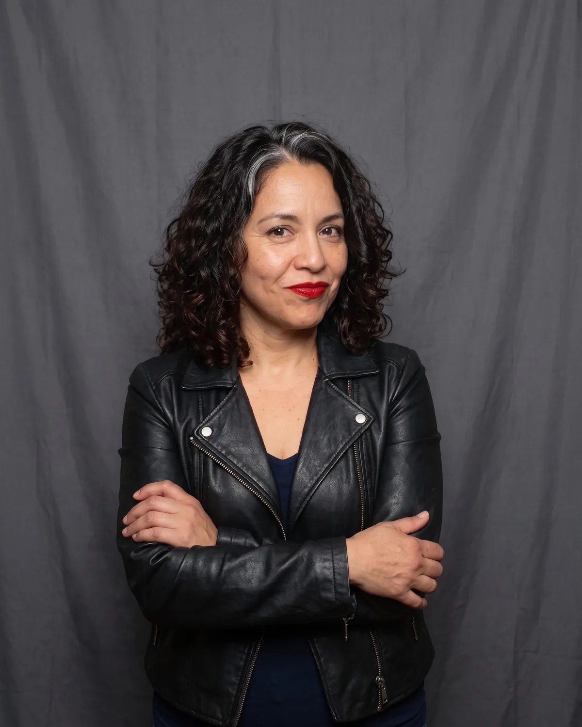 Guest at a company anniversary party in a leather jacket, arms crossed with a knowing smirk