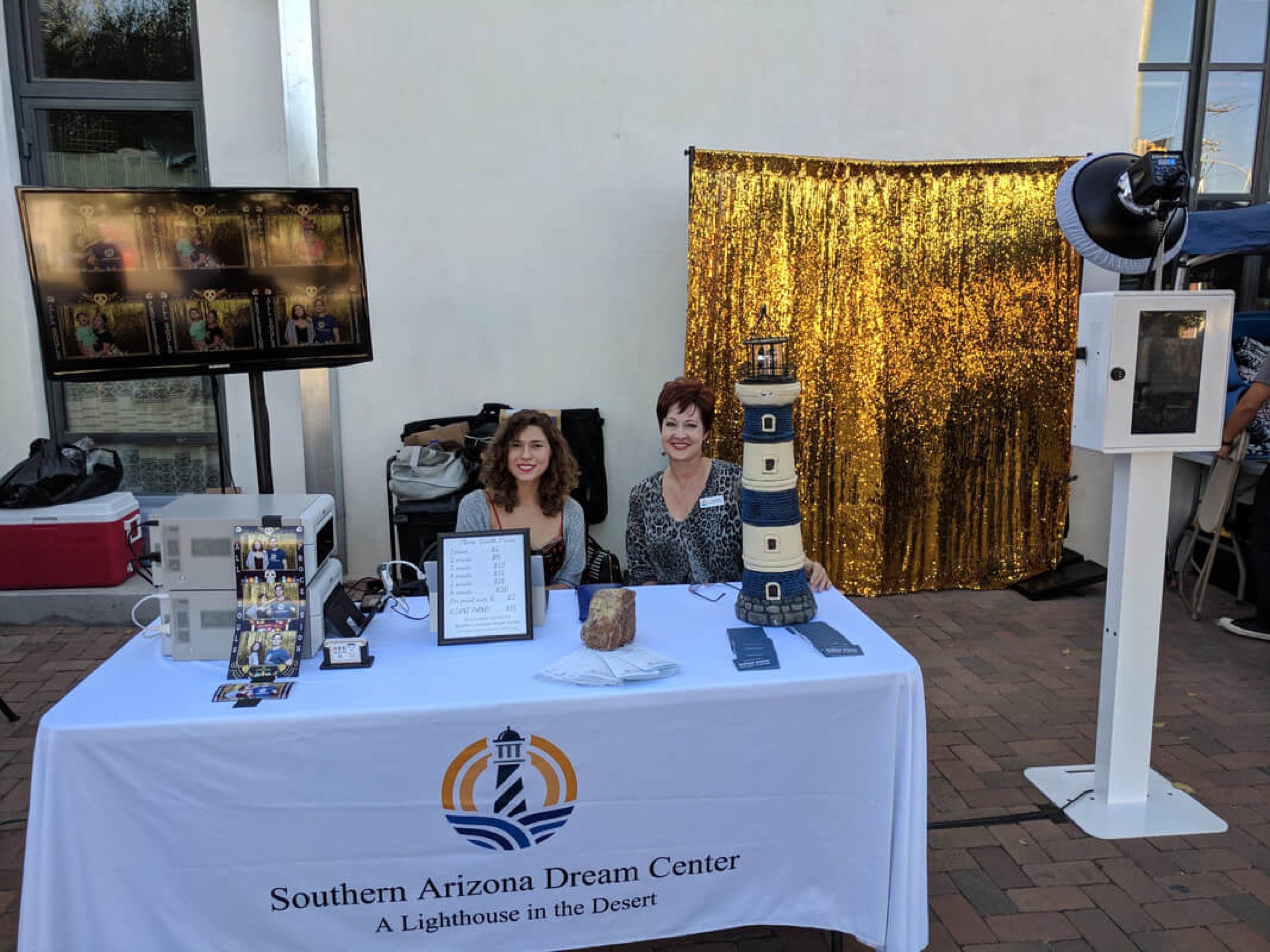 The 2017 All Souls Procession in Tucson — the booth set up with the Southern Arizona Dream Center, gold sequin backdrop, print station, and a live slideshow of the night's photos