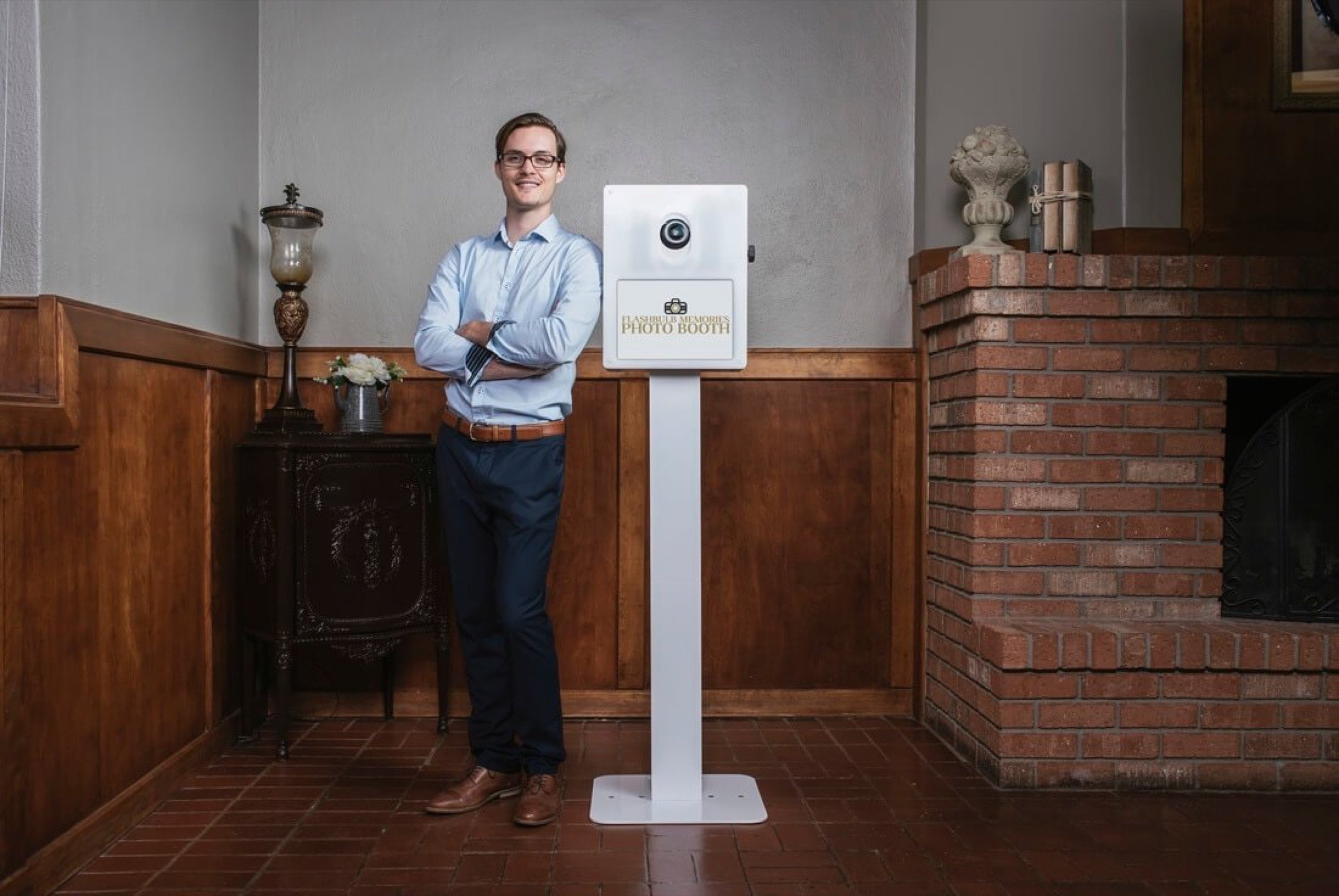Flashbulb Memories founder Matt standing beside the company's white powder-coated photo booth in a wood-paneled room