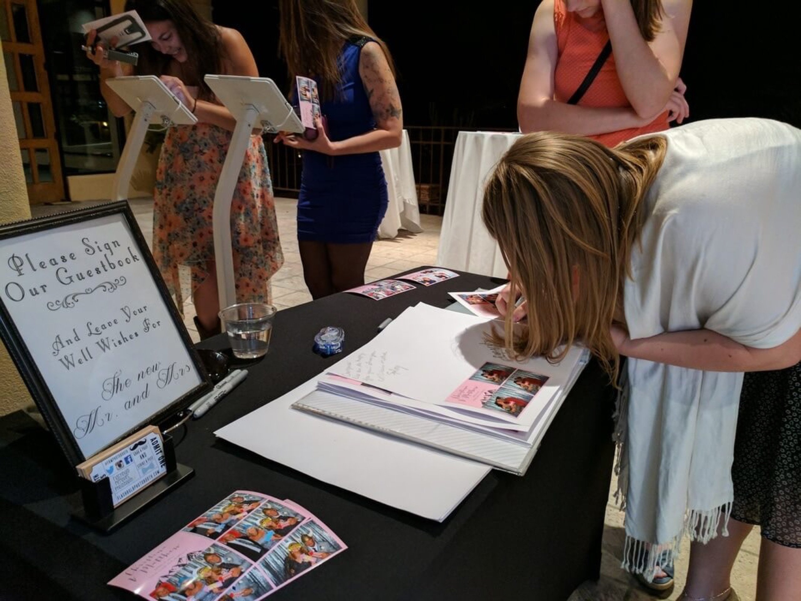 A guest signing the photo memory book beside a 'Please Sign Our Guestbook' frame at Christina and Matthew's wedding at the Omni, April 8, 2017
