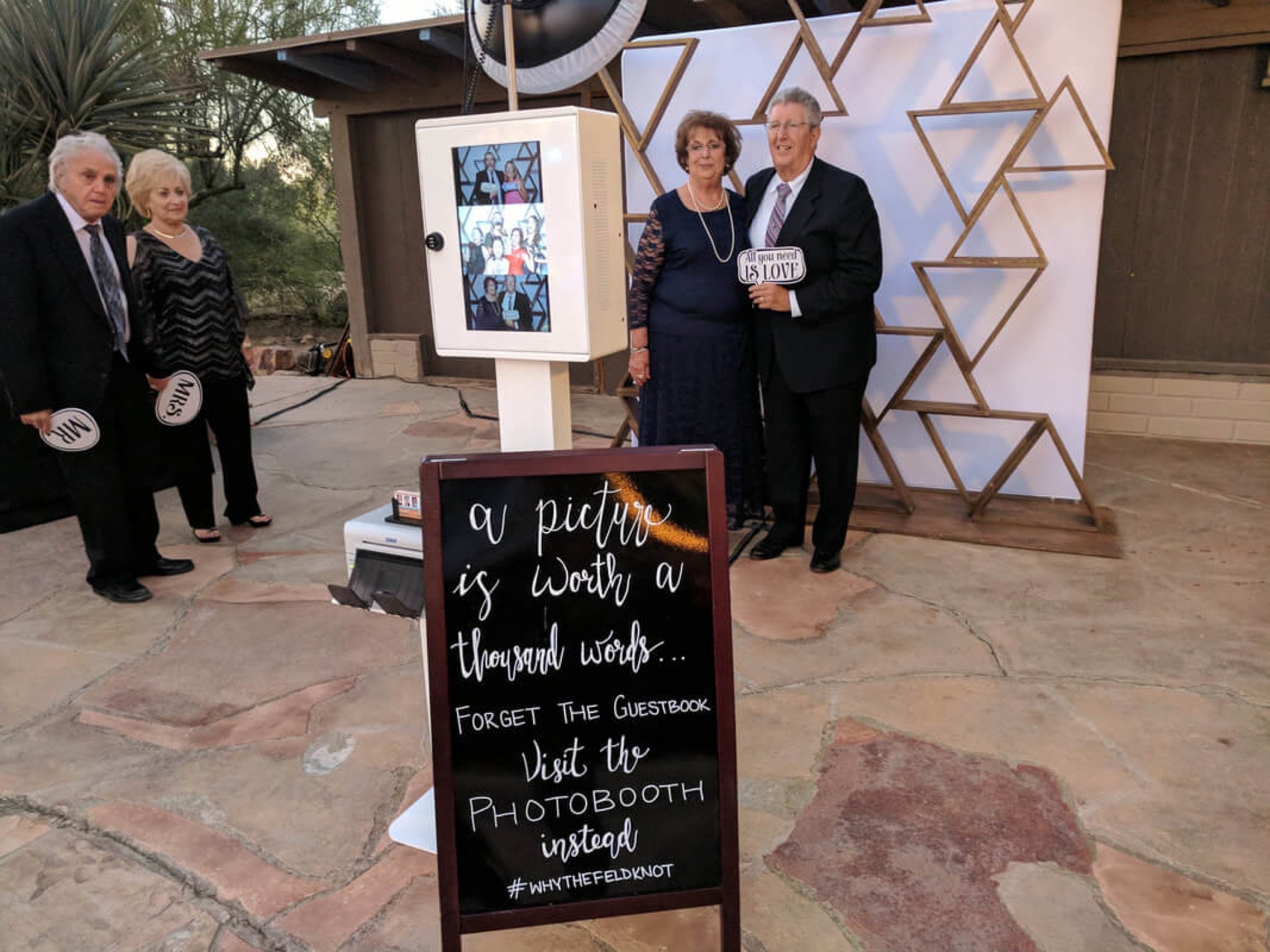 Guests posing beside the photo booth and a chalkboard sign reading 'forget the guestbook, visit the photobooth instead' at David and Abigail's wedding at Wild Horse Ranch, October 29, 2017