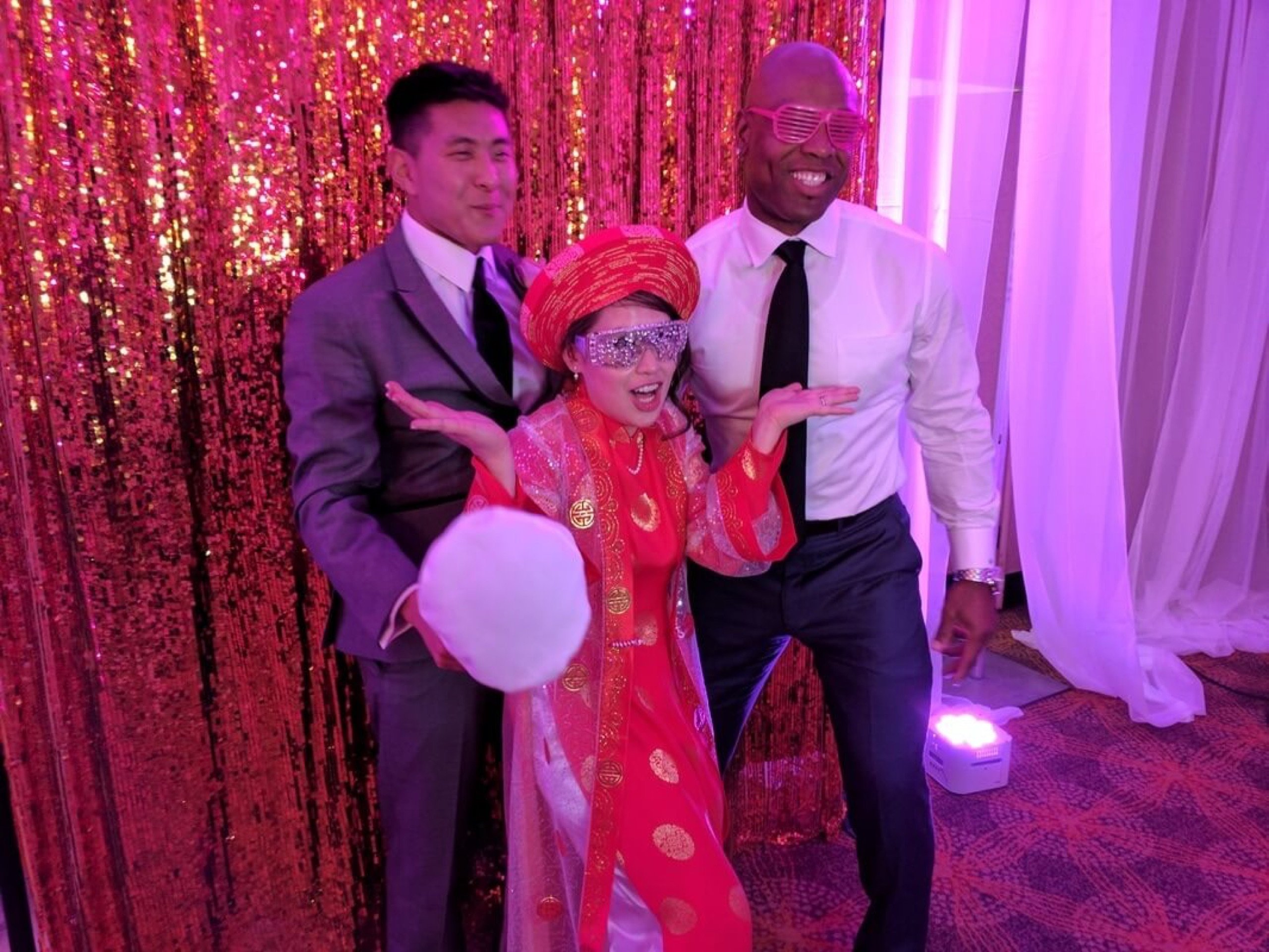 Wedding guests in glasses and props in front of a red sequin backdrop at Maria and Stanley's wedding at Hotel Tucson City Center, May 13, 2017