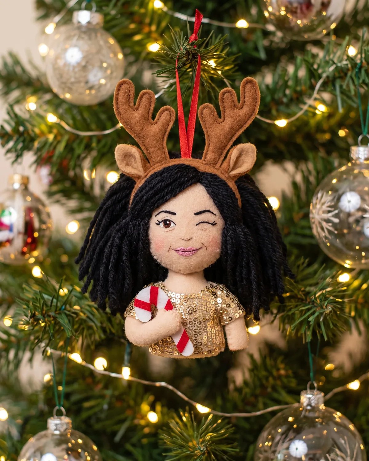 Plush doll ornament of the guest in antlers and a sequin top hanging on a decorated tree