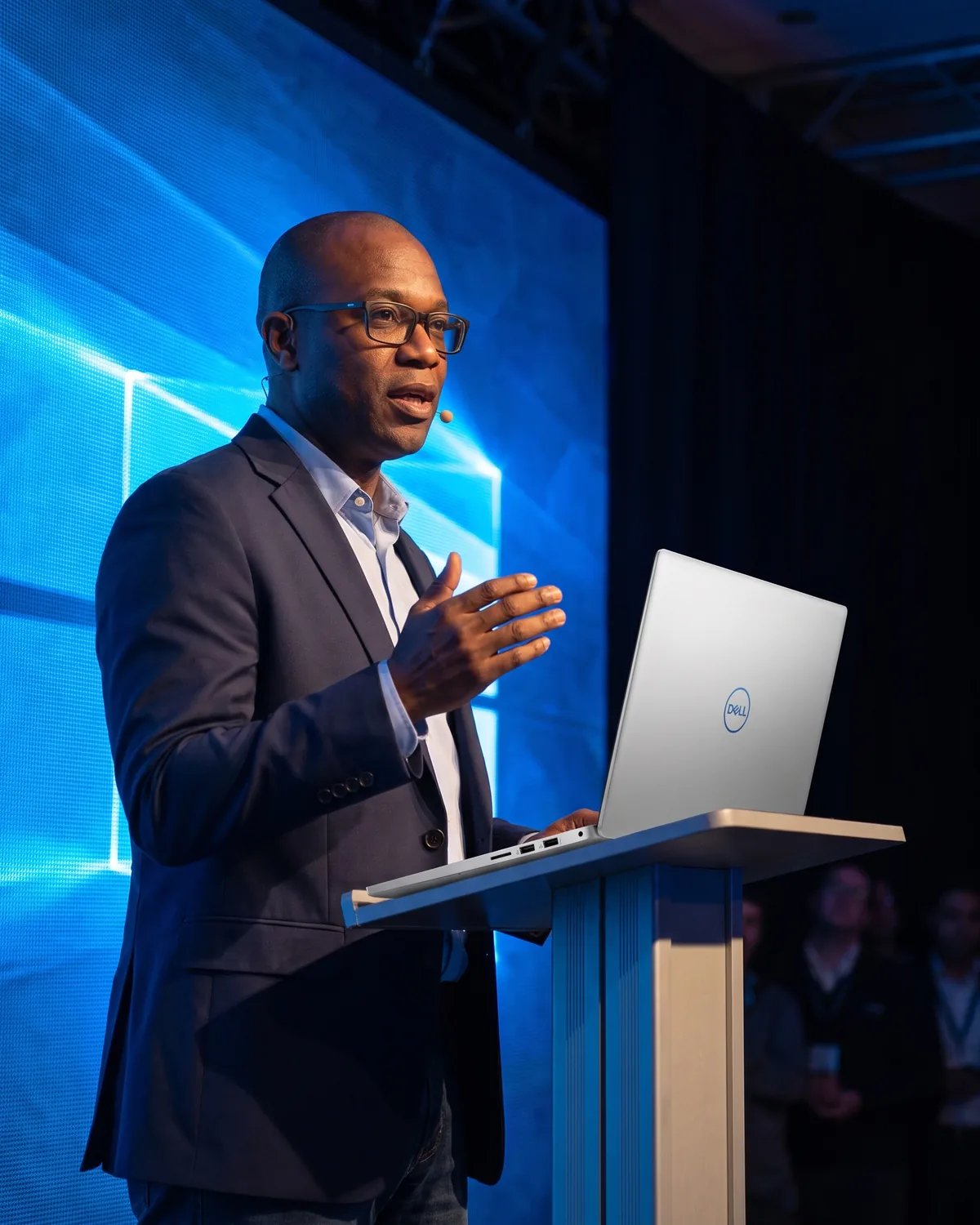 The attendee presenting on a keynote stage with a Dell laptop on the podium