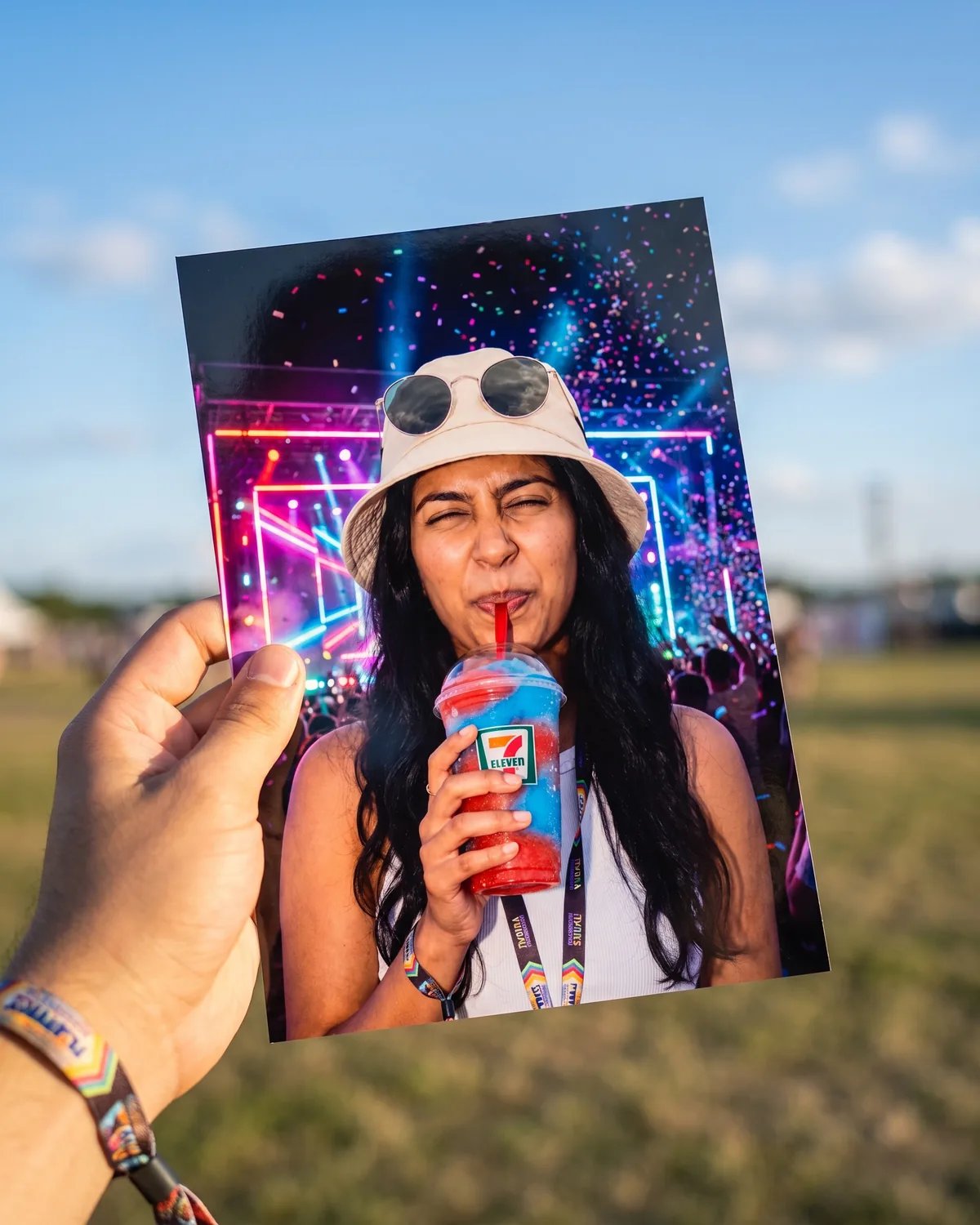 A guest holding up a print of the 7-Eleven festival photo in an open festival field