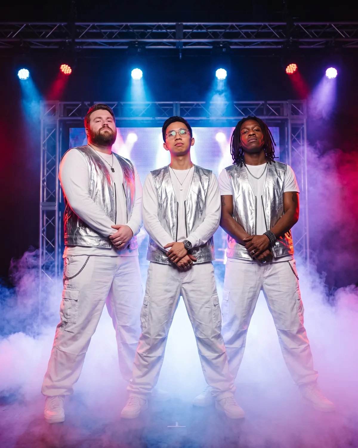 The three friends as a 1990s boy band in matching white outfits on a smoky stage
