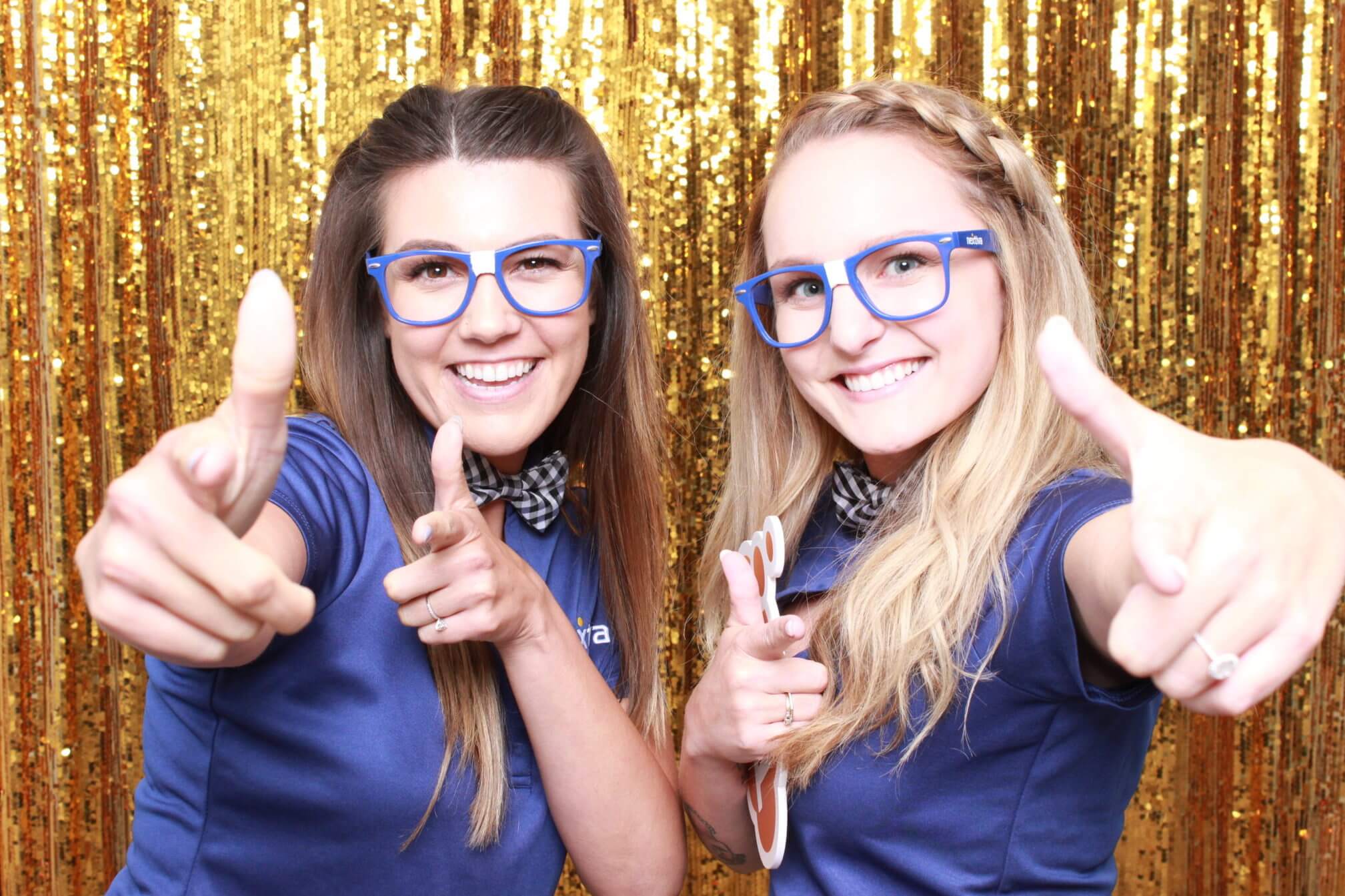 Two guests posing with prop glasses in front of a gold sequin photo booth backdrop