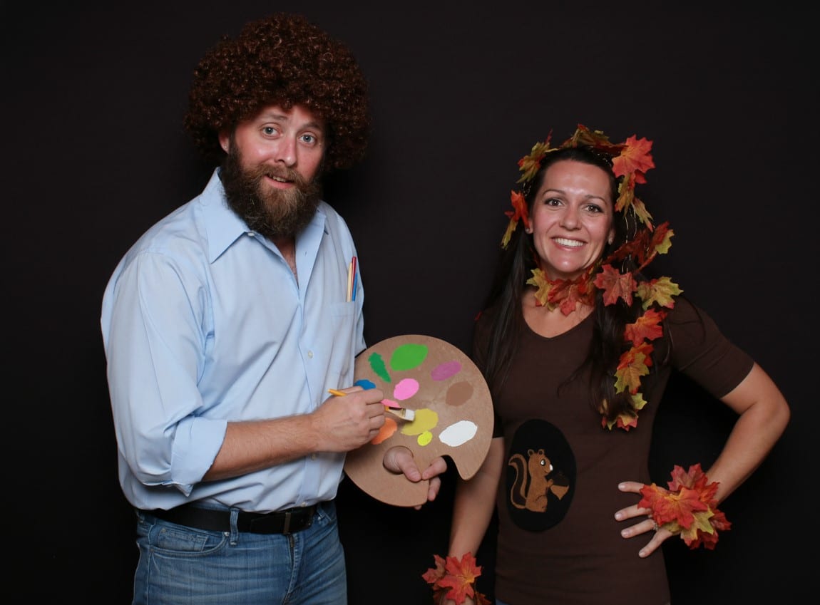Two guests in costume posing in front of a solid black photo booth backdrop