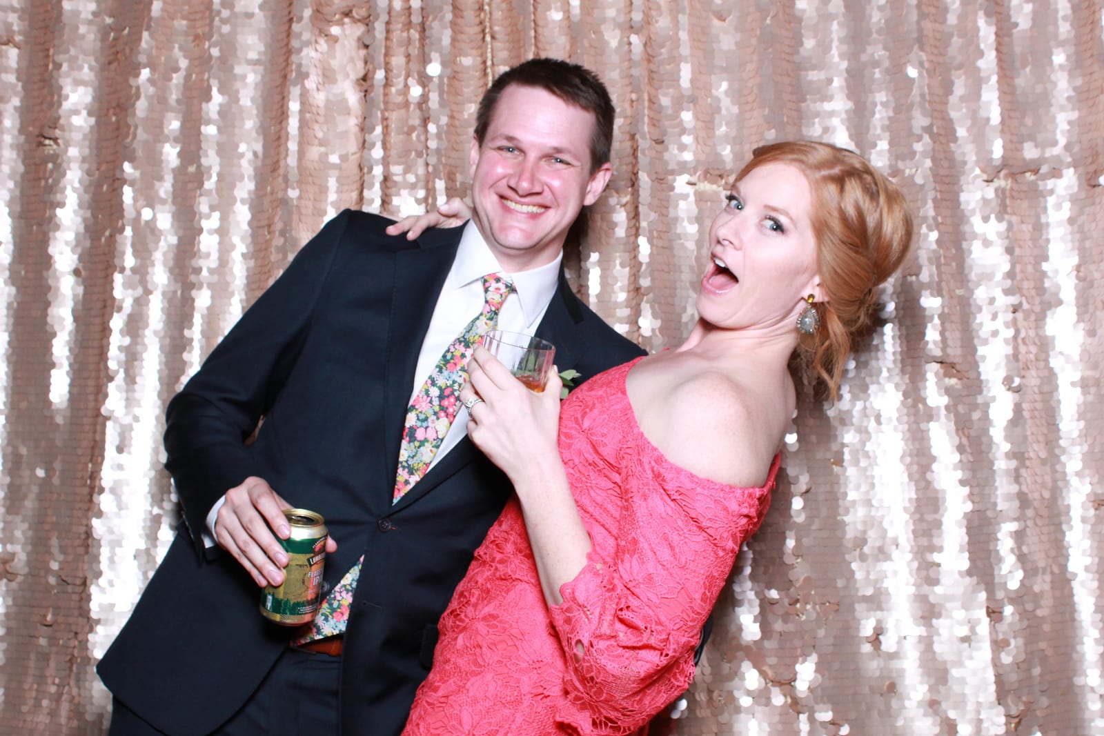 A couple posing in front of a blush sequin photo booth backdrop at a wedding