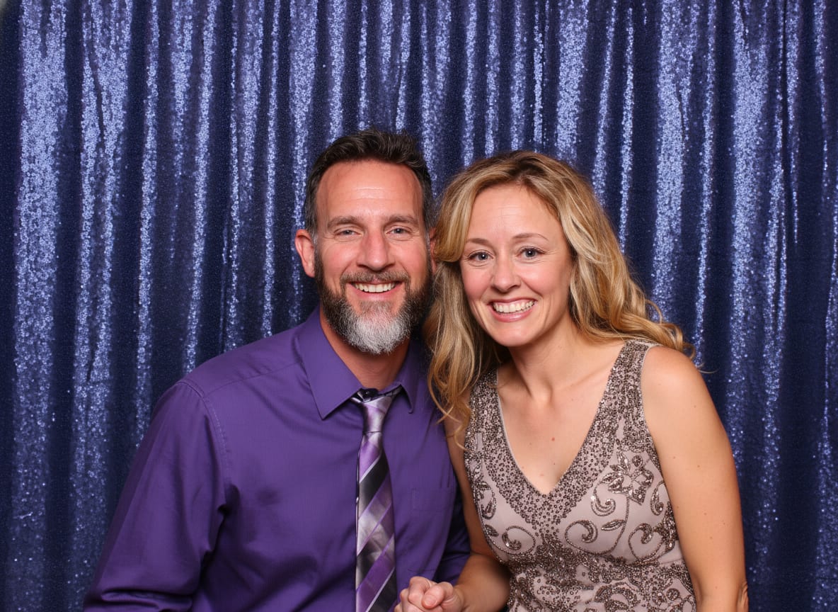 A couple in formal attire in front of a navy sequin photo booth backdrop