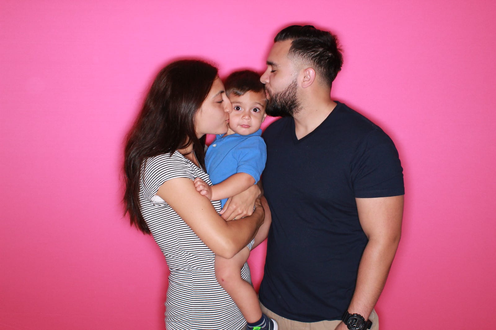 A family with a toddler posing against a hot pink photo booth backdrop