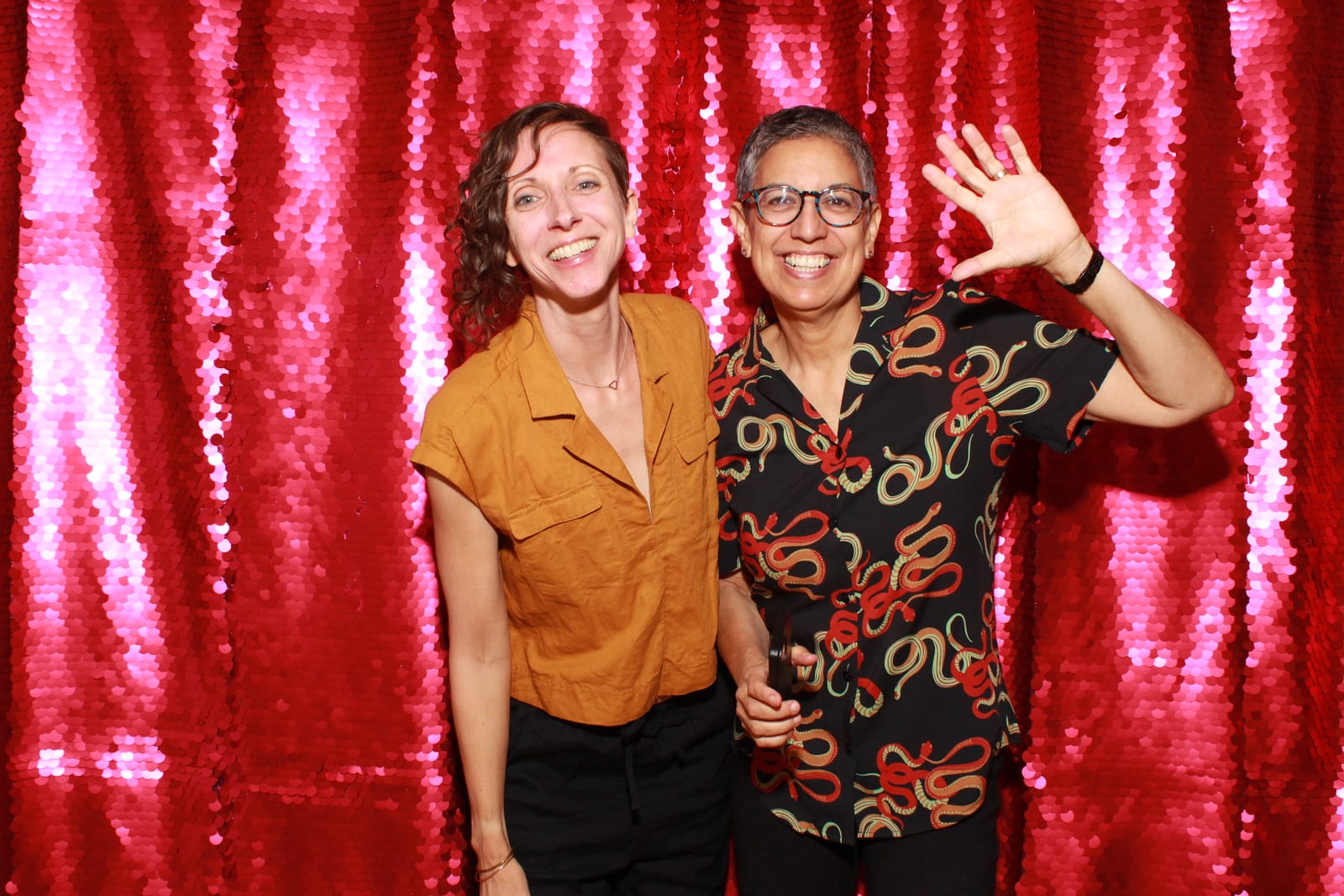 Two guests posing in front of a pink sequin photo booth backdrop