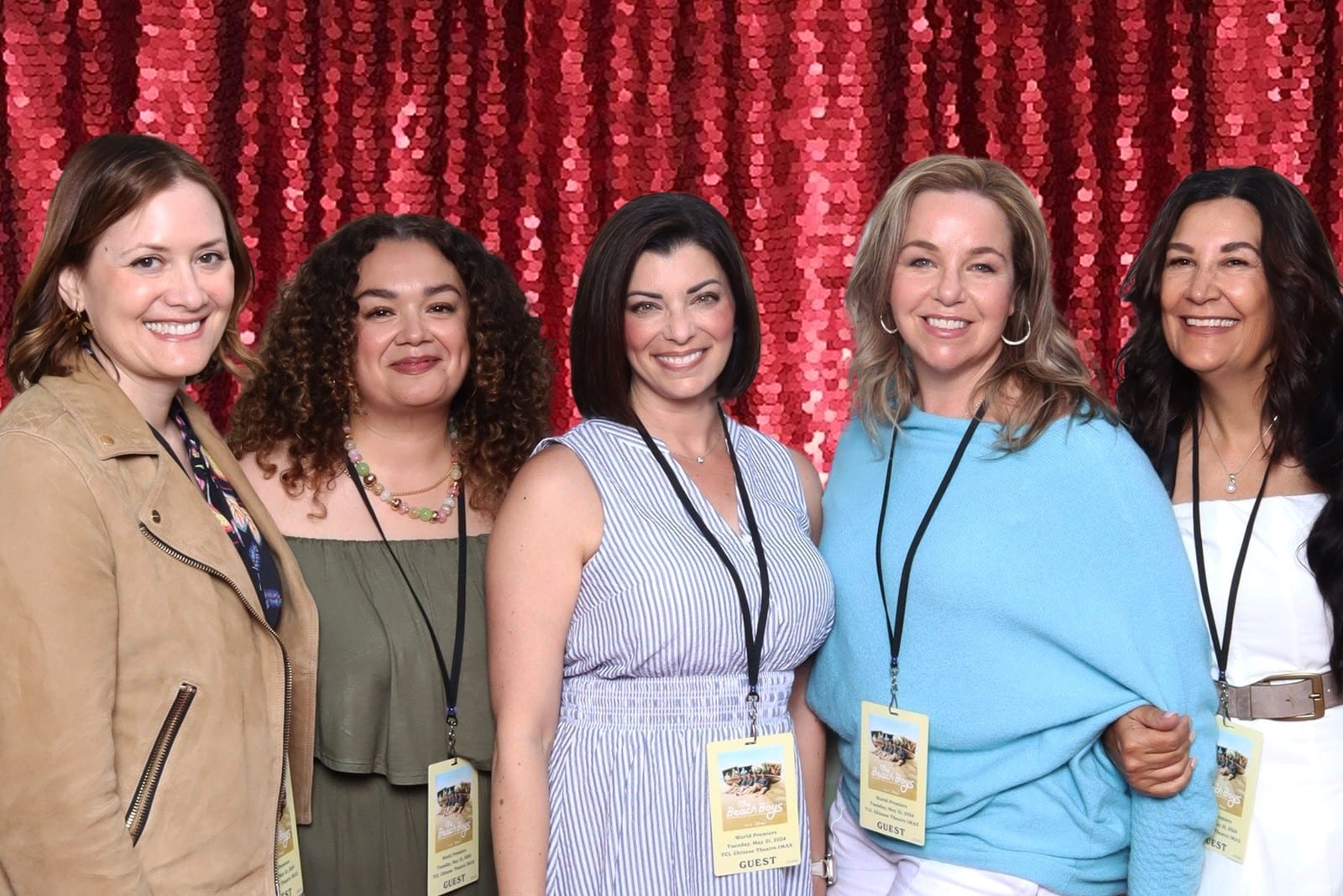 A group of conference attendees posing against a red sequin photo booth backdrop