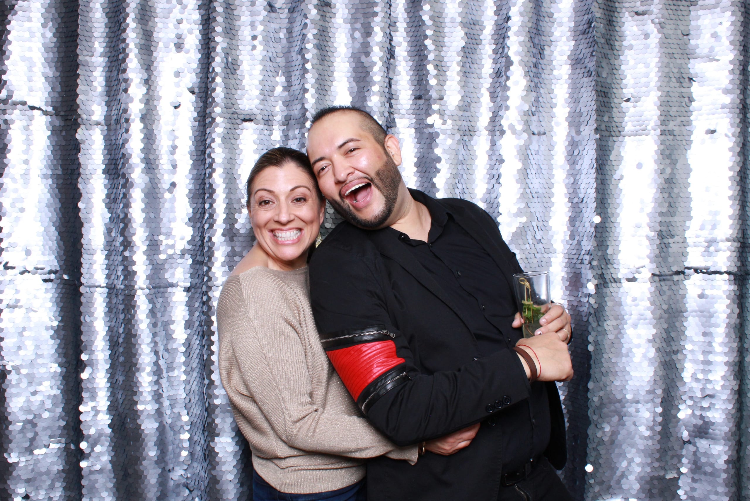 A couple posing in front of a silver sequin photo booth backdrop