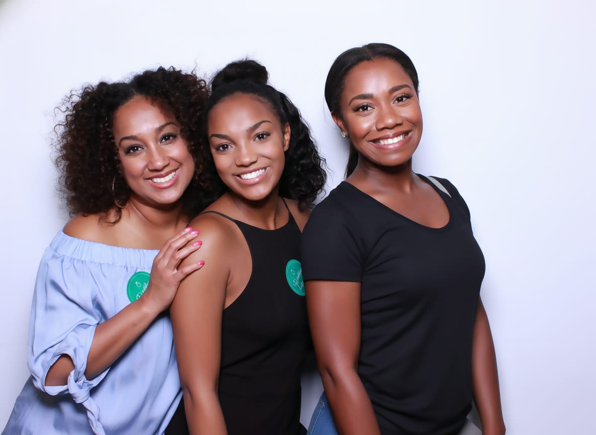 Three guests laughing in front of a white photo booth backdrop