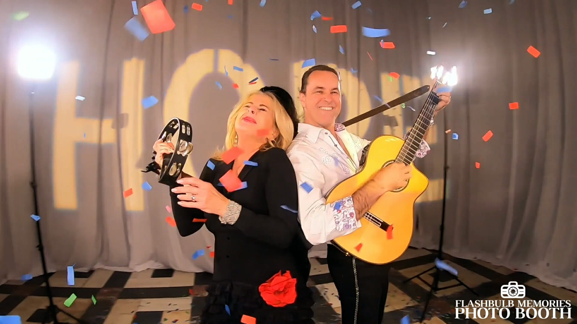 A couple posing back to back with a guitar and tambourine as confetti falls around them