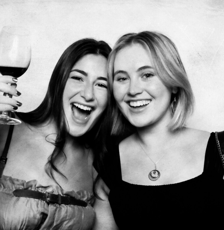 Two friends laughing with a glass of wine in a black and white vintage booth portrait